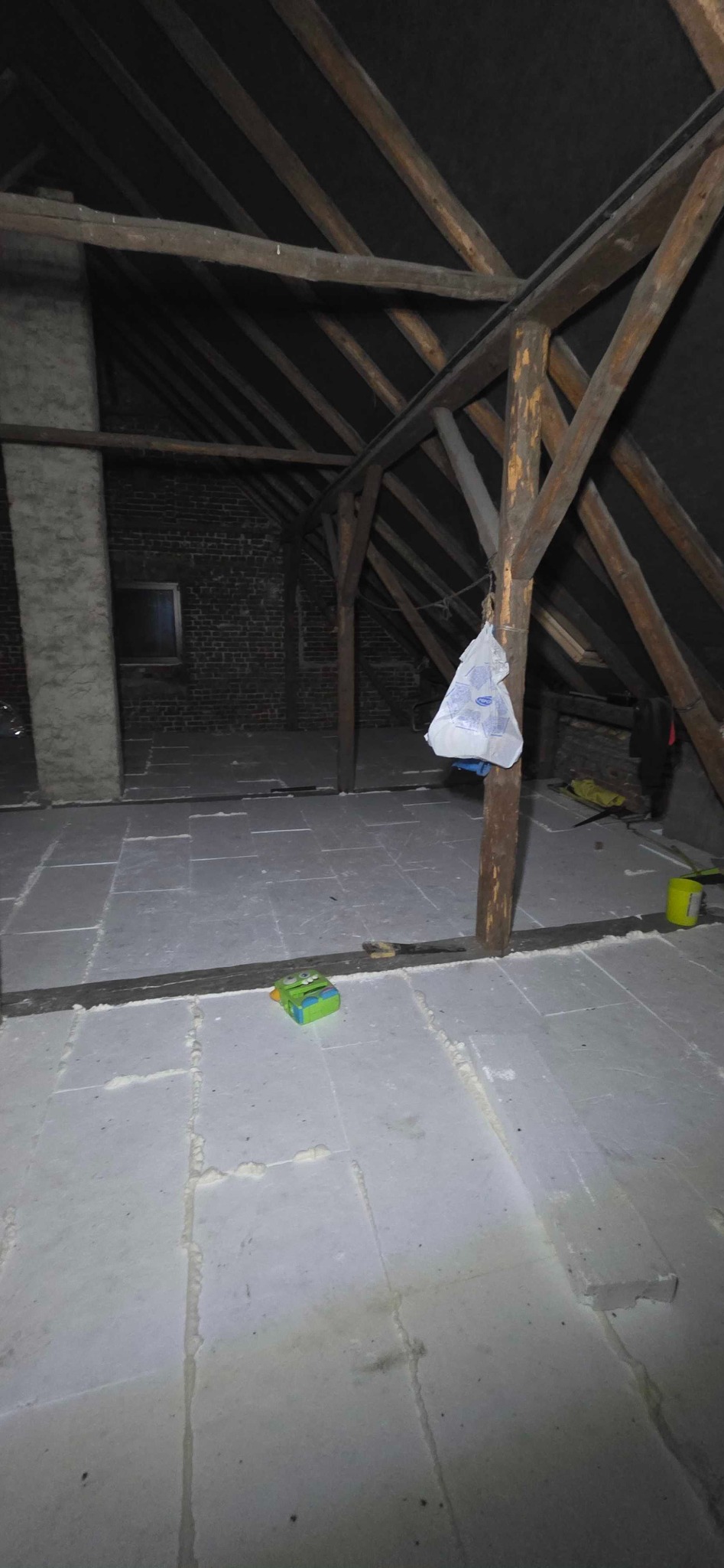 Poddasze z drewnianą konstrukcją i ułożonymi płytami izolacyjnymi. Widoczne szczeliny wypełnione pianką montażową, narzędzia i akcesoria budowlane.