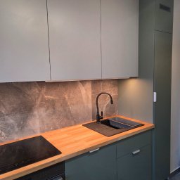 MEBLE ADOZ JAKUB PERZANOWSKI - Nowoczesna kuchnia z szarymi szafkami górnymi i zielonymi dolnymi, drewnianym blatem, czarną armaturą i marmurowym panelem. Minimalistyczny design z oświetleniem podszafkowym.