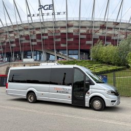 NikoTour - Nowoczesny srebrny bus NikoTour z otwartymi drzwiami, zaparkowany przed Stadionem Narodowym PGE Narodowy w Warszawie, gotowy do przewozu.