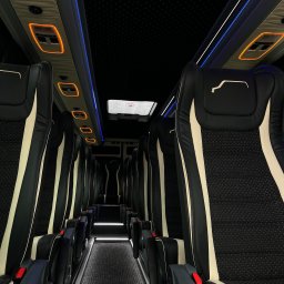 NikoTour - Eleganckie wnętrze busa z rzędami czarno-kremowych foteli, ambientowym niebieskim oświetleniem LED i pomarańczowymi panelami. Podświetlany korytarz i 'gwieździsta' podsufitka.