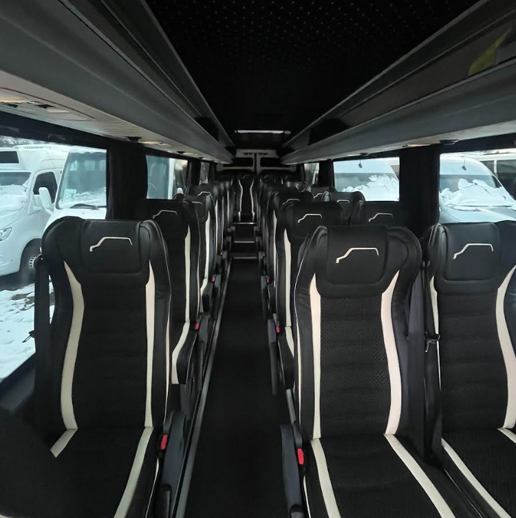 Wnętrze komfortowego busa z czarnymi skórzanymi fotelami z białymi wstawkami, widok z przodu na puste siedzenia, za oknem zimowy krajobraz.