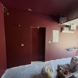 D.M. Daniel Maciejowski - Pomieszczenie po malowaniu ścian i sufitu na bordowo. Widoczne niedociągnięcia przy podłodze i niezabezpieczone kable. W tle brama garażowa.