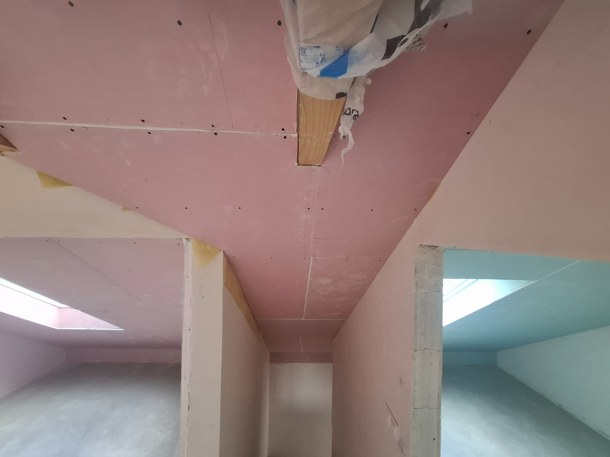 Montaż płyt karton-gips na suficie w nowo wykończonym wnętrzu. Widoczne łączenia płyt i drewniane elementy konstrukcyjne. Surowy stan wykończenia, przygotowanie do malowania.