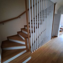 Estica Produkcja i Usługi Stolarskie - Nowoczesne schody z drewnianymi stopniami i białymi podstopnicami, z ażurową balustradą z pionowych białych listew i drewnianą poręczą.