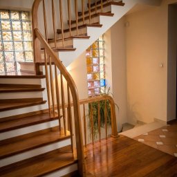 Estica Produkcja i Usługi Stolarskie - Eleganckie, zakręcone schody z ciemnego drewna z białymi podstopnicami i drewnianą balustradą, oświetlone przez ścianę z barwnych luksferów.