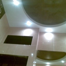 Art.Profil - Wykończona łazienka z beżowymi płytkami, dekoracyjnym wzorem na ścianie i podwieszanym sufitem z okrągłym elementem. Widoczne oświetlenie punktowe.