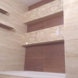 Art.Profil - Wykończona łazienka z beżowymi i brązowymi płytkami, nad wanną półki z dekoracyjnym wzorem. Widok na fragment ściany i wanny, bez armatury.