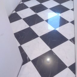 Art.Profil - Ukończona podłoga w szachownicę z czarno-białych płytek marmurowych, ułożonych pod kątem w małej łazience. Widoczne odbicie światła na powierzchni płytek.