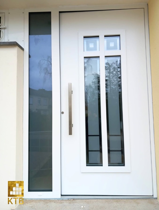 Białe drzwi wejściowe z przeszkleniami, pionowy uchwyt ze stali nierdzewnej, widoczne odbicie otoczenia w szybach, nowoczesny design.