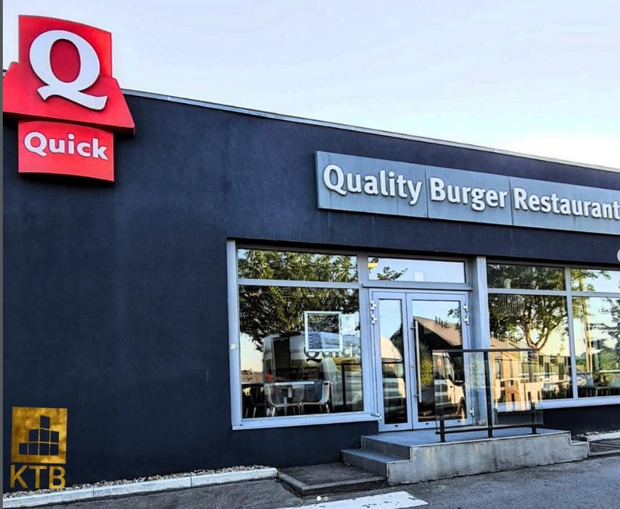 Elewacja restauracji z dużymi oknami i logo 'Quick' oraz 'Quality Burger Restaurant'. Widoczne schody wejściowe i logo firmy KTB w rogu.