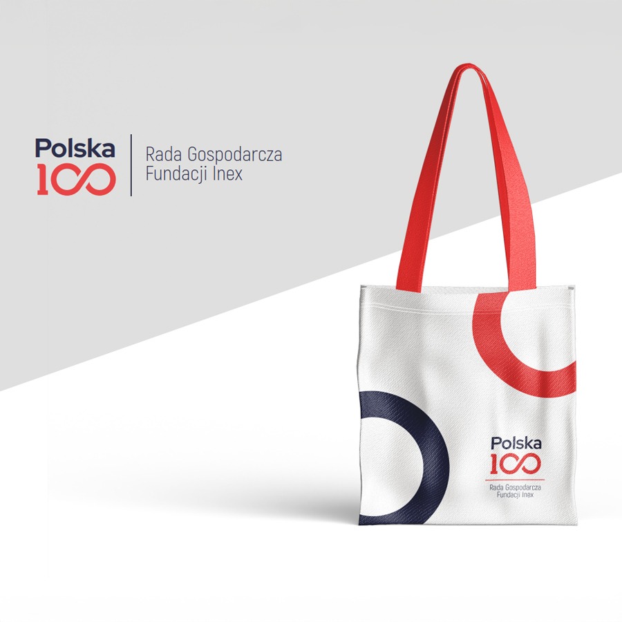 Biała torba bawełniana z czerwonymi uchwytami i logo 'Polska 100' w kolorach czerwonym i granatowym, na jasnoszarym tle z cieniem.