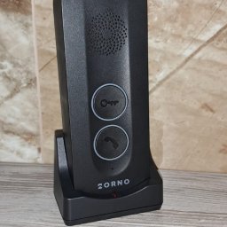 ELEKTROSOLUTIONS KAMIL JUDKA - Czarny, nowoczesny wideodomofon ZORNO na podstawce, z przyciskami klucza i słuchawki, na tle marmurowej ściany i drewnianego blatu. Minimalistyczny design.