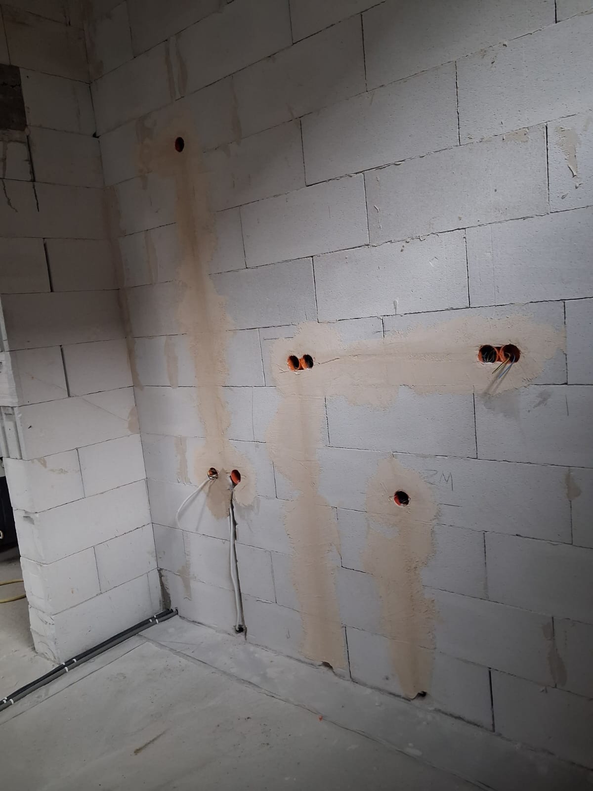 Ściana z betonu komórkowego z wywierconymi otworami i wystającymi przewodami elektrycznymi, przygotowana do dalszych prac wykończeniowych.