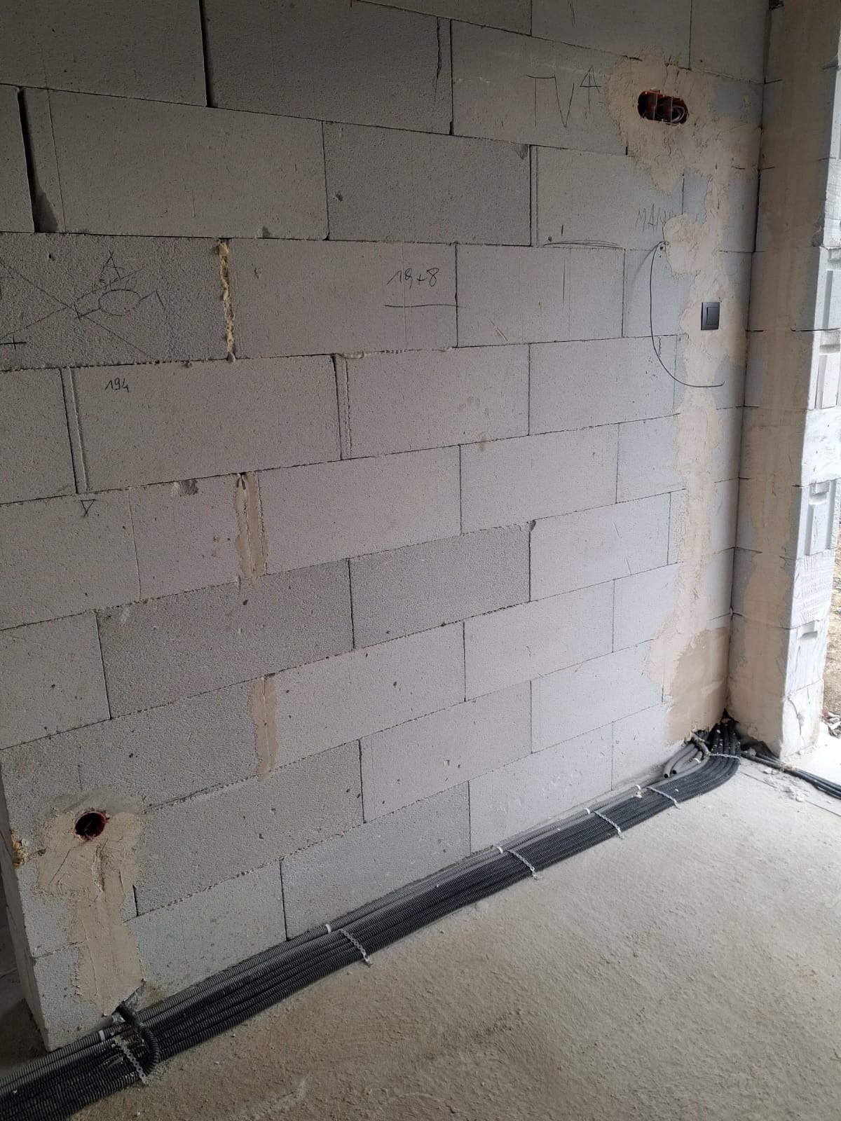 Ściana z betonu komórkowego z widocznymi przewodami elektrycznymi w peszlach, przygotowanymi do rozprowadzenia instalacji. Widoczne puszki i włącznik.