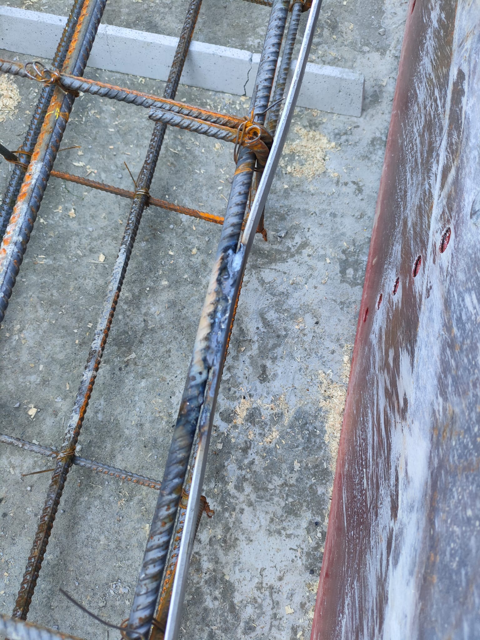 Zbrojenie fundamentu z widocznymi prętami, drutem wiązałkowym i deskowaniem. Elementy konstrukcyjne przygotowane do zalania betonem, widoczne ślady korozji na prętach.