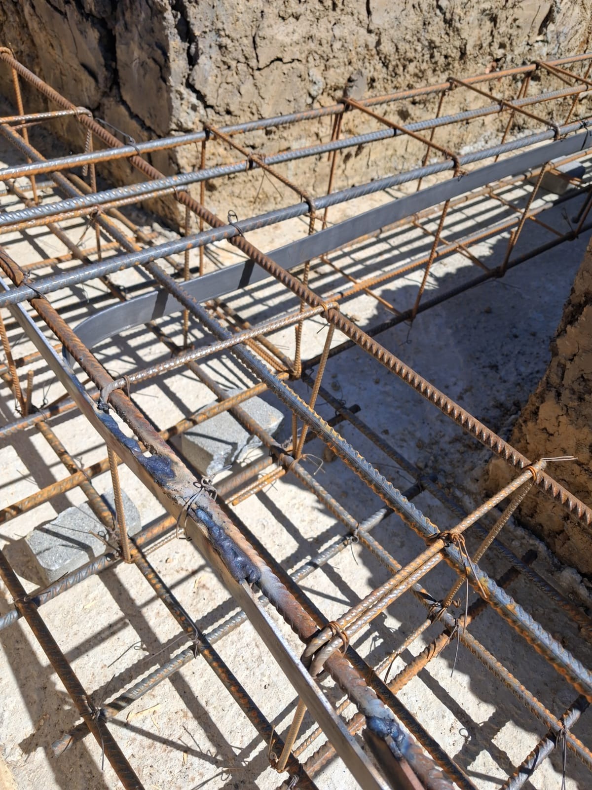 Zbrojenie fundamentów z widocznymi spawami i elementami stalowymi, przygotowane do zalania betonem. Widok z góry na siatkę zbrojeniową w wykopie.