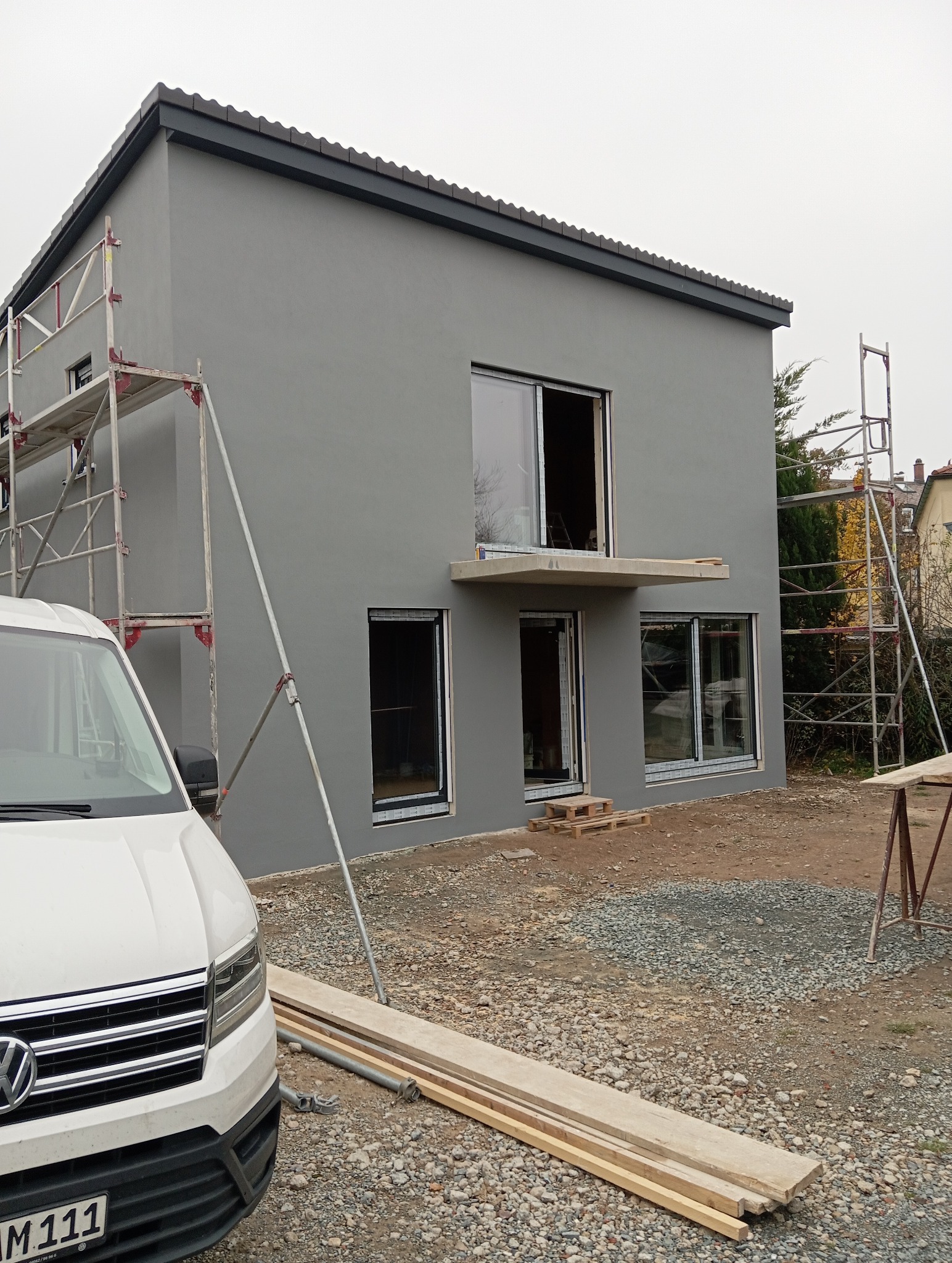 Szara elewacja domu jednorodzinnego w Zielonej Górze po tynkowaniu, z widocznymi rusztowaniami i częściowo zamontowanymi oknami. Nowoczesny styl.