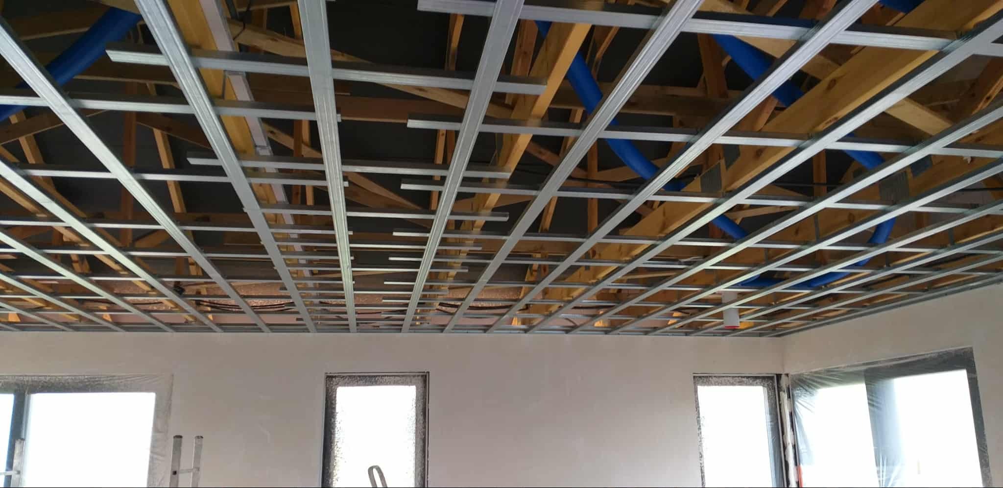 Sufit podwieszany z metalową konstrukcją i instalacją wentylacyjną w nowym budynku. Widoczne drewniane elementy konstrukcyjne dachu.