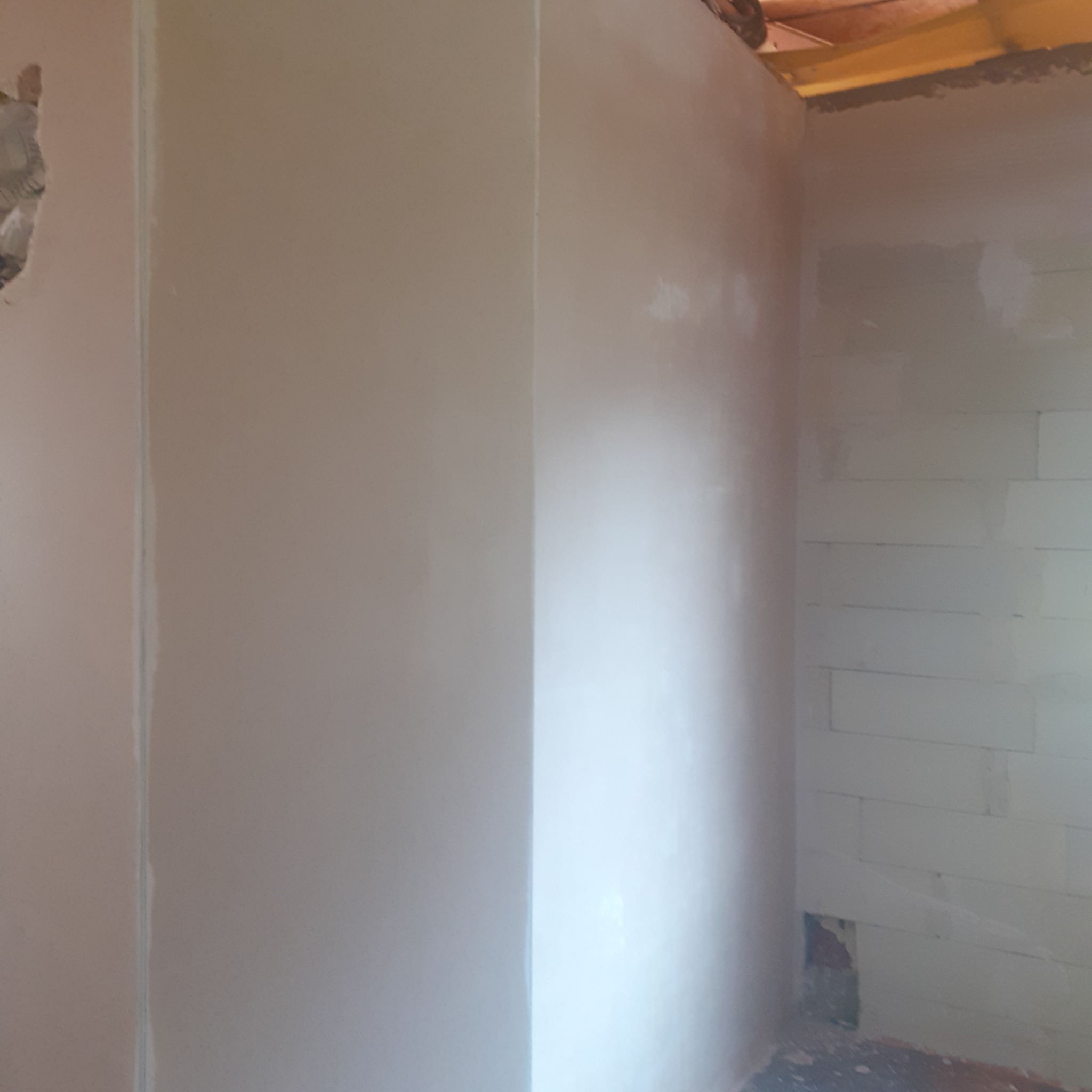 Świeżo położony, jasny tynk na ścianie wewnętrznej, widoczne bloczki z betonu komórkowego na sąsiedniej ścianie. Fragment drewnianej konstrukcji dachu w rogu.