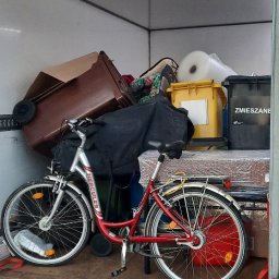 Daniel Szentes - Wnętrze busa załadowane rzeczami do przeprowadzki, w tym rower, kartony, worki i pojemniki. Widoczna tablica rejestracyjna pojazdu.