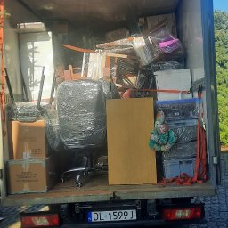 Daniel Szentes - Wnętrze busa wypełnione meblami i kartonami, przygotowanymi do transportu. Widoczne krzesło biurowe owinięte folią, skrzynie i inne przedmioty. Tablica rejestracyjna DL 1599J.