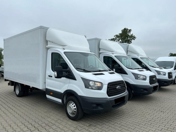 Flota białych samochodów dostawczych Ford Transit z zabudową kontenerową, ustawionych w rzędzie na parkingu. Widok z boku na pierwszy pojazd.