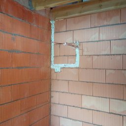 IK Klimat Ivan Ivanieiev - Murowana ściana z pustaków ceramicznych z wyciętym i uszczelnionym otworem na instalację elektryczną. Widoczne przewody. Surowy stan.