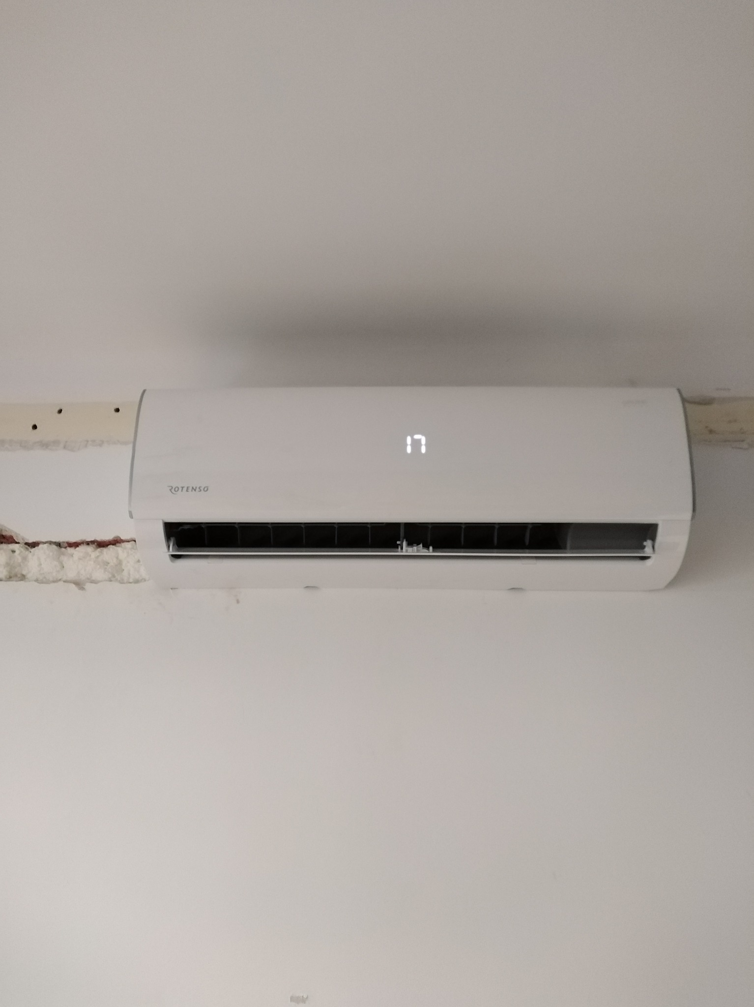 Biały klimatyzator Rotenso na ścianie, wyświetlający temperaturę 17 stopni, z widoczną pianką montażową wokół urządzenia. Minimalistyczny design, proste linie.