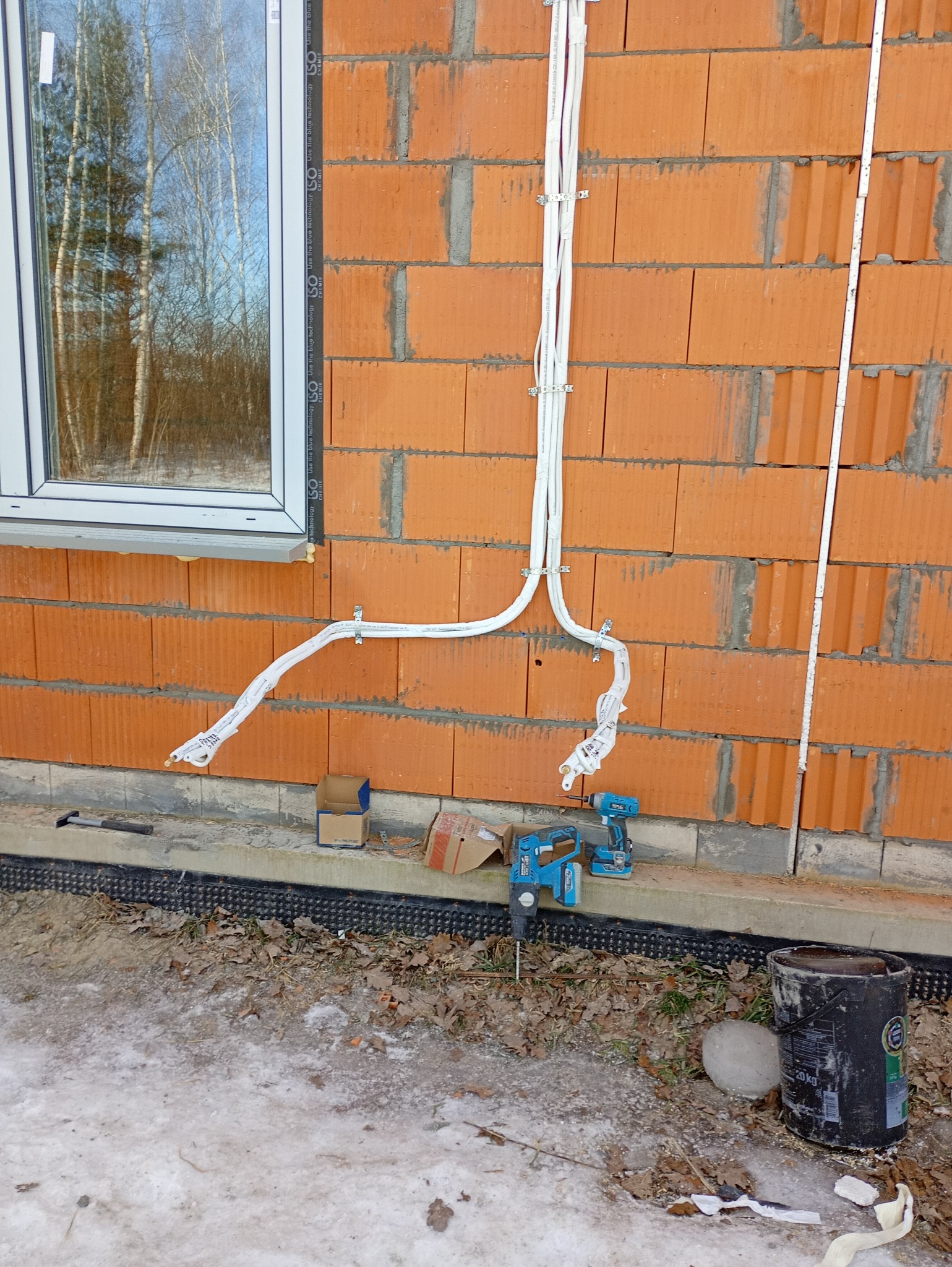 Montaż instalacji freonowej klimatyzacji na ceglanej ścianie budynku w trakcie budowy. Widoczne narzędzia i materiały instalacyjne.