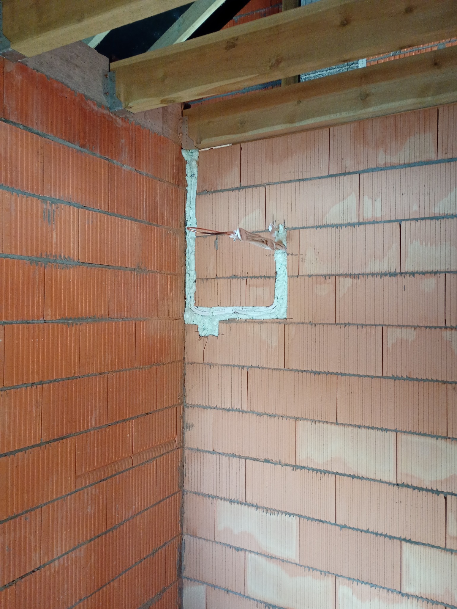 Murowana ściana z pustaków ceramicznych z wyciętym i uszczelnionym otworem na instalację elektryczną. Widoczne przewody. Surowy stan.
