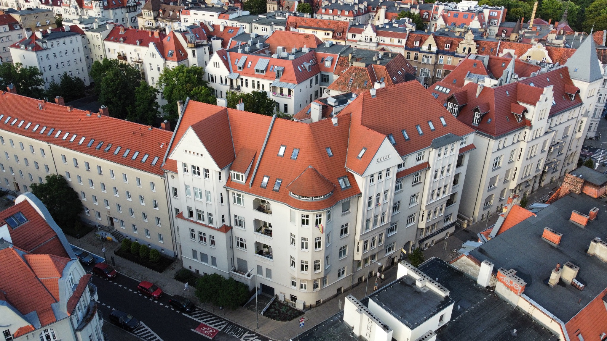 Panorama miasta z lotu ptaka, prezentująca budynki mieszkalne z czerwonymi dachami i jasnymi elewacjami. Widok na architekturę miejską z góry, z perspektywy drona.