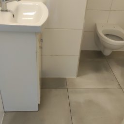 ShinEx Cleaning Service - Czysta, minimalistyczna łazienka z białą umywalką, toaletą i płytkami. Widoczne ślady po umyciu podłogi, podkreślające świeżość i dbałość o detale.