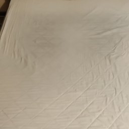 ShinEx Cleaning Service - Czysty, biały materac na łóżku z szarym zagłówkiem. Widoczne pikowania w romby na materacu. Neutralne oświetlenie.