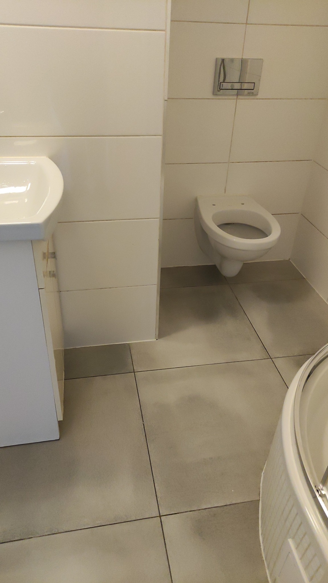 Czysta, minimalistyczna łazienka w Sosnowcu z wiszącą toaletą, umywalką i szarymi płytkami podłogowymi. Widok na świeżo umytą podłogę i armaturę.