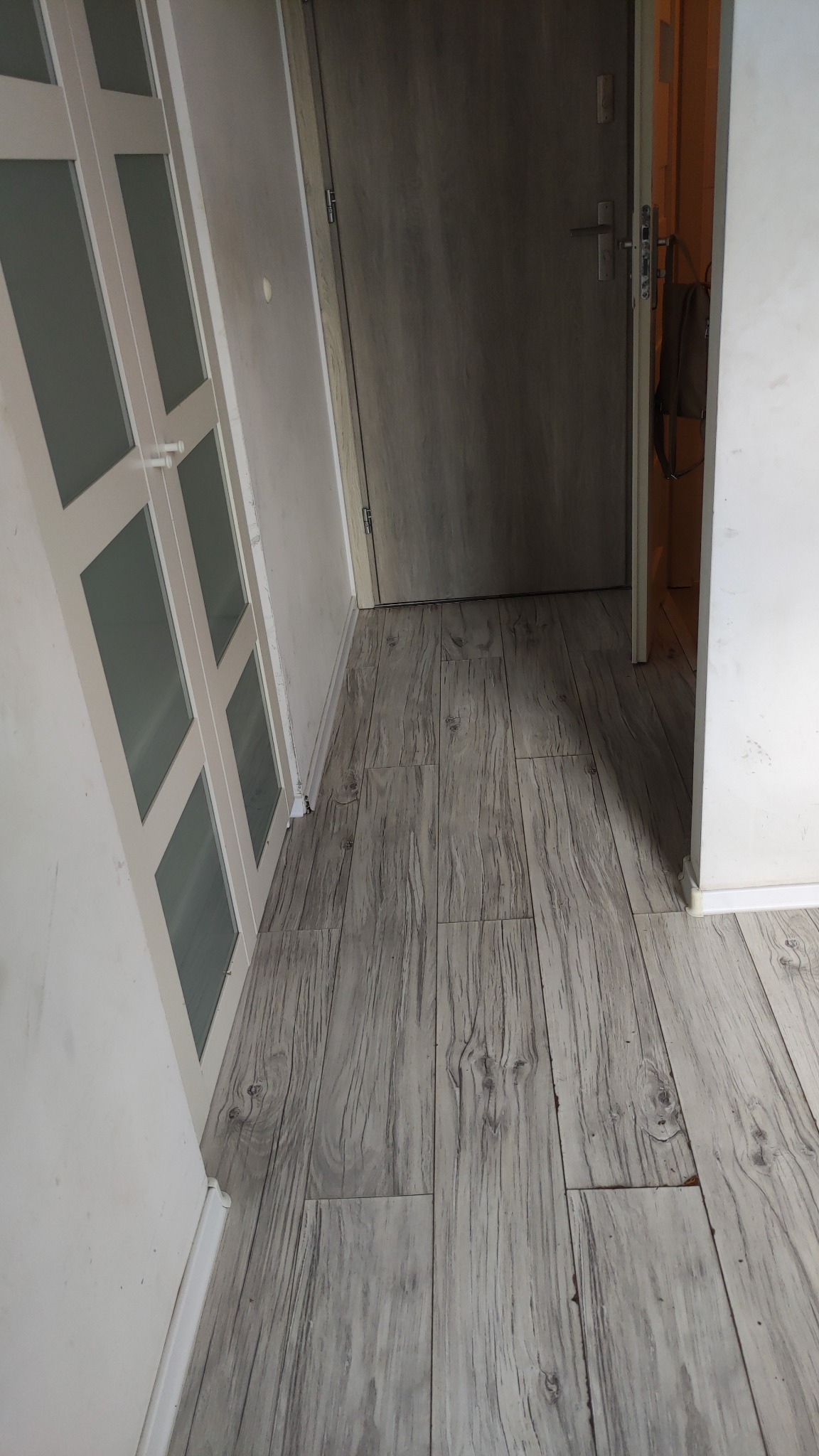 Ułożona podłoga z paneli imitujących drewno w korytarzu, widok z góry, drzwi wejściowe i szafa w tle. Jasne wnętrze po remoncie.