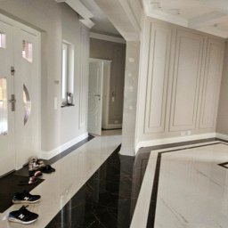 Paweł Sabiun - Elegancki hol z błyszczącą, czarno-białą marmurową podłogą w geometryczny wzór. Ściany w odcieniach szarości z dekoracyjnymi panelami i listwami.