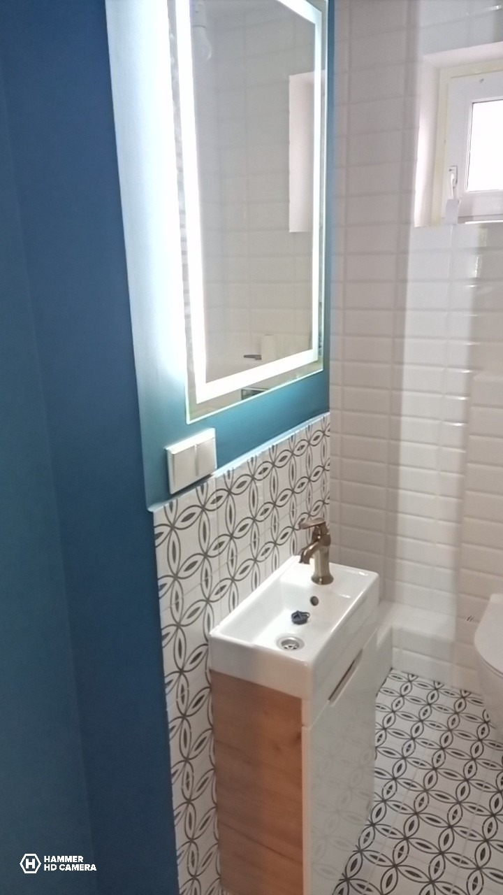 Nowoczesna łazienka z umywalką na szafce z drewnianym frontem, lustrem z podświetleniem LED i wzorzystymi płytkami na ścianie i podłodze.