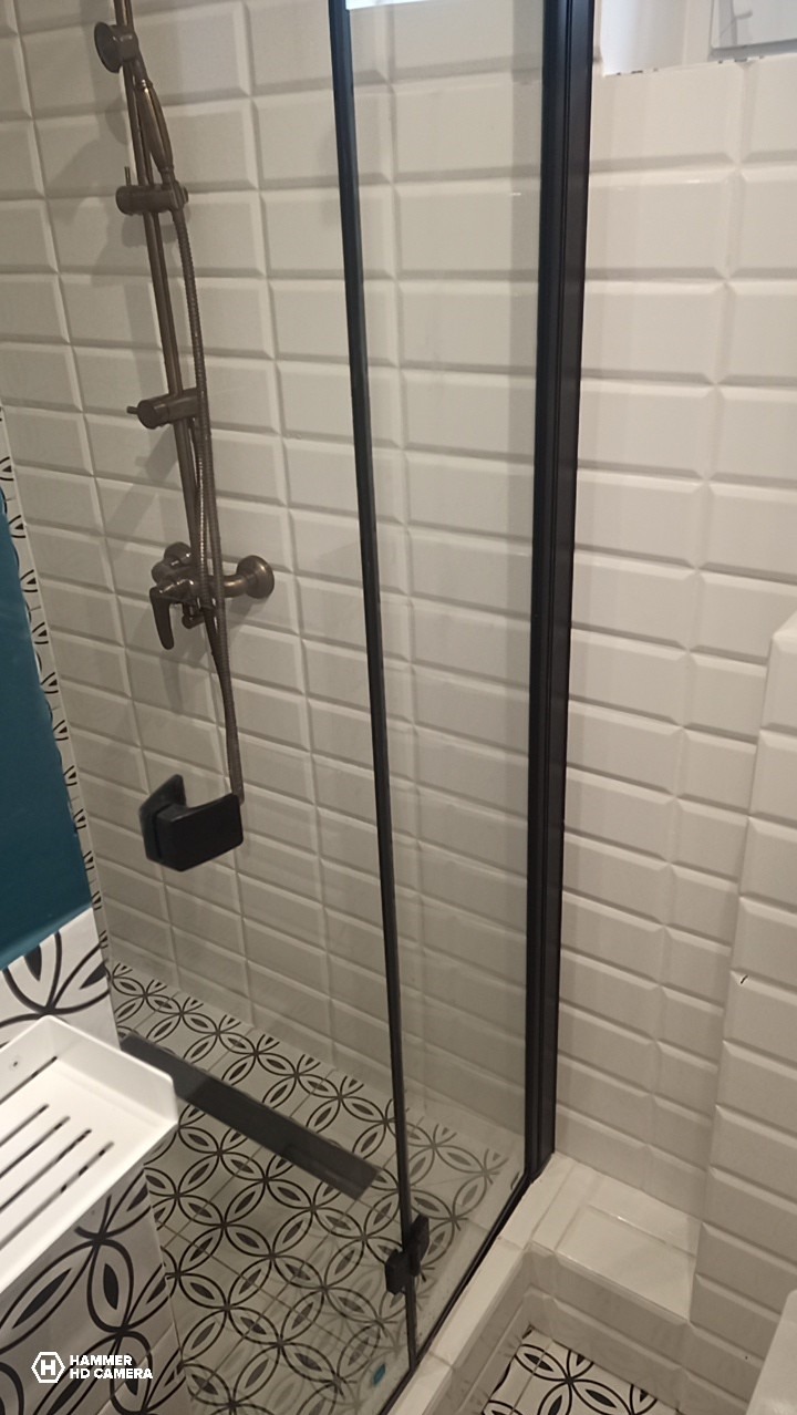 Nowoczesna kabina prysznicowa z czarnymi profilami i armaturą w kolorze starego złota, wykończona białą cegiełką i wzorzystą mozaiką podłogową.