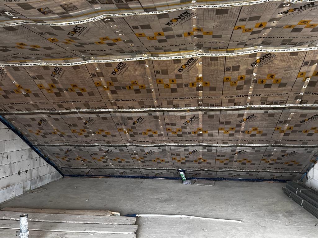 Poddasze z widoczną folią paroizolacyjną Isover, przygotowane do dalszych prac wykończeniowych. Widoczne elementy konstrukcyjne i materiały budowlane.