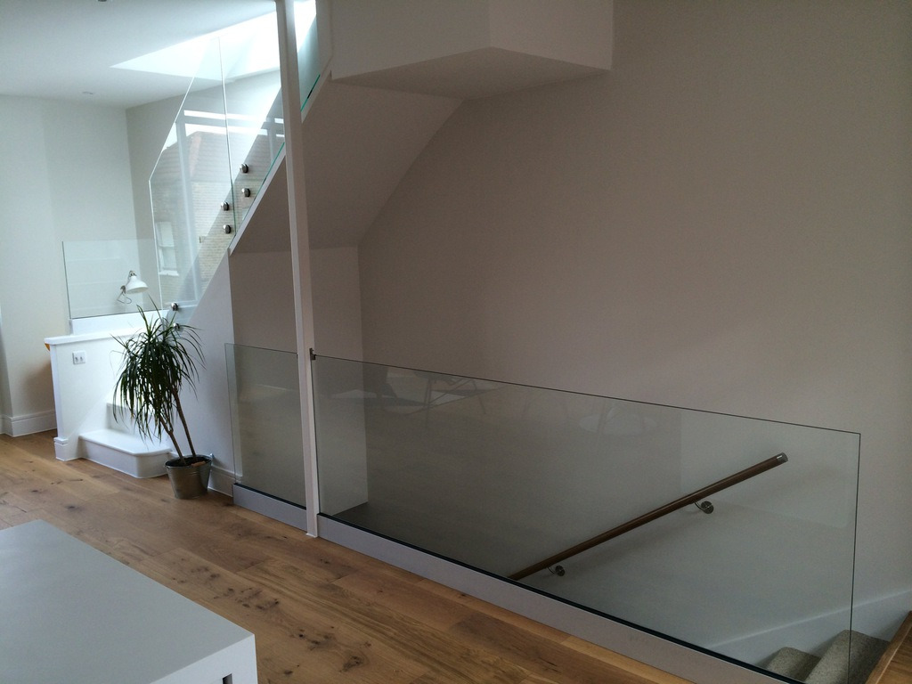 Nowoczesne schody z szklaną balustradą i drewnianą poręczą, oświetlone światłem dziennym z okna dachowego. Minimalistyczny design, jasne wnętrze, drewniana podłoga.