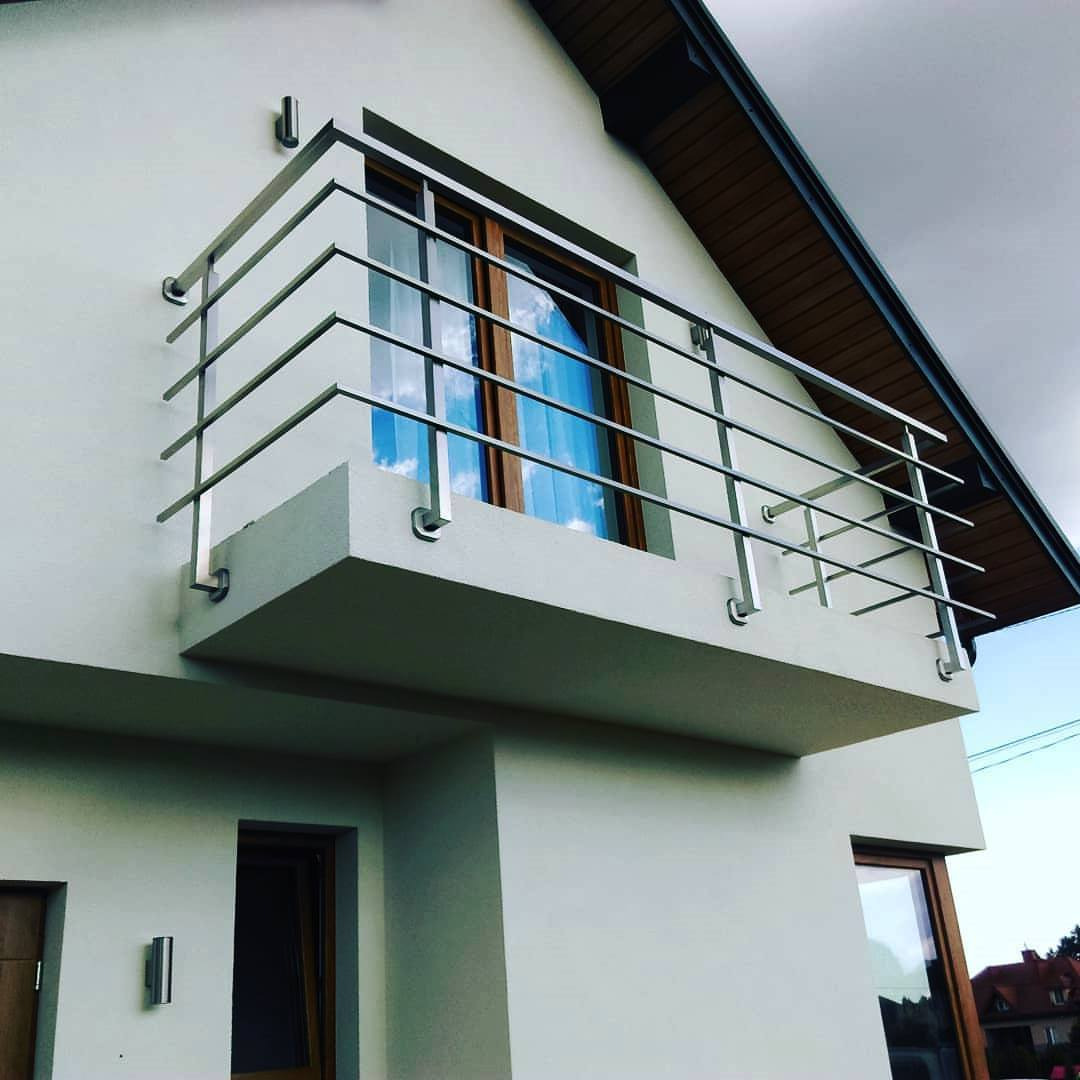 Nowoczesna balustrada balkonowa ze stali nierdzewnej w Jabłonnie. Minimalistyczny design, poziome pręty, jasna elewacja budynku, widok z dołu.