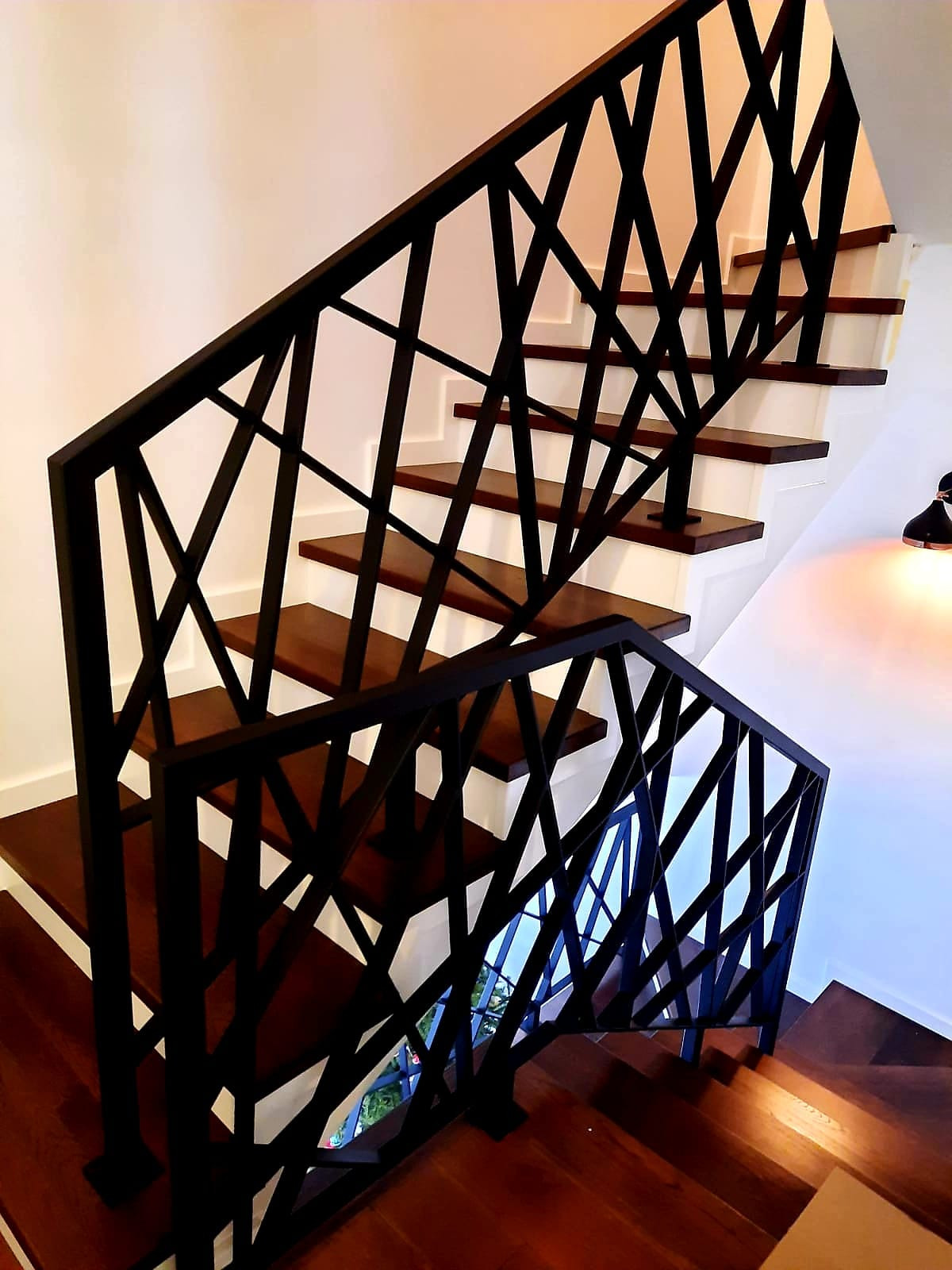 Nowoczesne schody drewniane z czarną, geometryczną balustradą metalową. Widok z dołu, podkreślający unikalny design i solidne wykonanie.