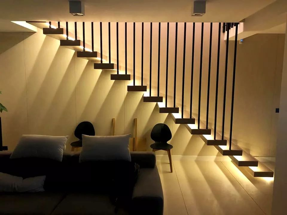Nowoczesne schody wspornikowe z podświetleniem LED, czarne balustrady pionowe. Minimalistyczny design w jasnym wnętrzu z sofą i krzesłami w tle.