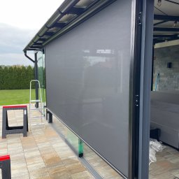 Masters - Rolety - Zewnętrzna roleta w kolorze szarym, zamontowana na tarasie z widoczną drabiną i narzędziami, sugerująca świeży montaż. Nowoczesny design i funkcjonalność.