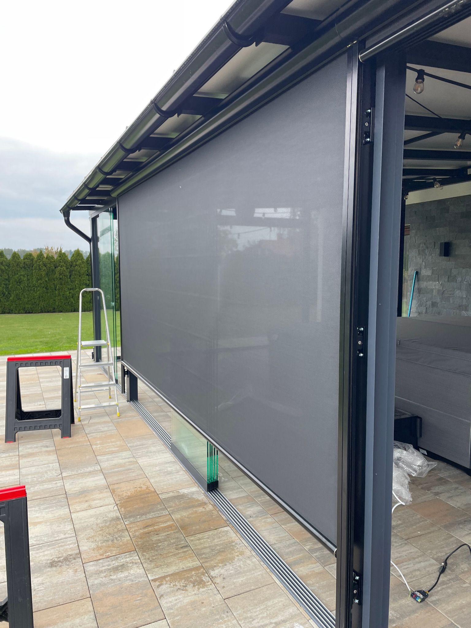 Zewnętrzna roleta w kolorze szarym, zamontowana na tarasie z widoczną drabiną i narzędziami, sugerująca świeży montaż. Nowoczesny design i funkcjonalność.