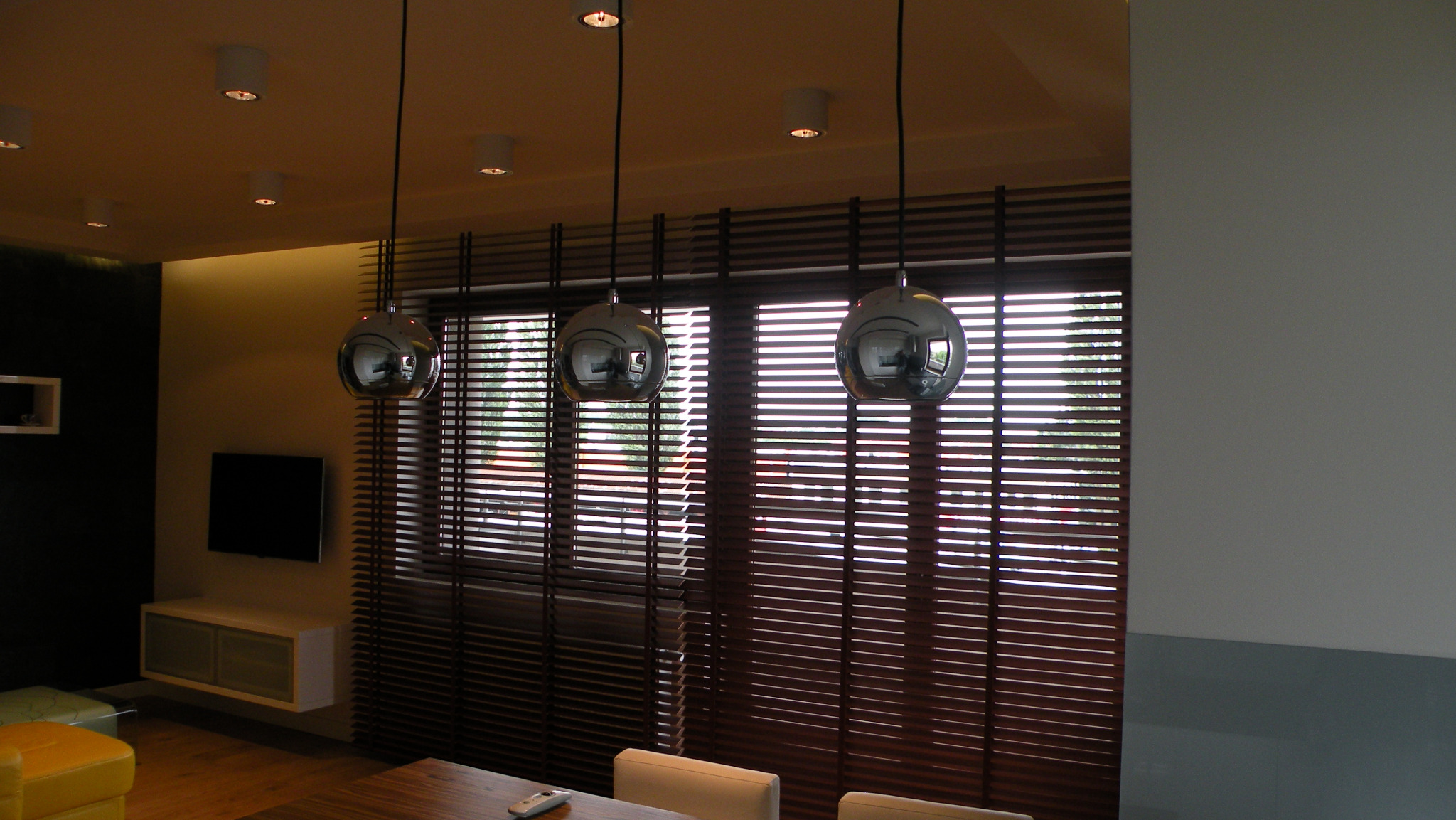 Brązowe żaluzje poziome w nowoczesnym wnętrzu, z trzema kulistymi lampami wiszącymi. Widok na zewnątrz przez okno. Minimalistyczny design.