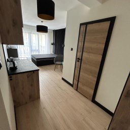 Well Done - Nowoczesne wnętrze: drewniana podłoga, drzwi z czarną ramą, aneks kuchenny z czarnym blatem, łóżko z wezgłowiem i czarne lampy wiszące. Minimalistyczny design.