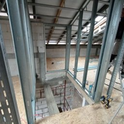 Well Done - Montaż metalowej konstrukcji szkieletowej na poddaszu, widoczne profile, płyty OSB, narzędzia. Prace wykończeniowe w surowym stanie, przygotowanie do dalszych etapów.