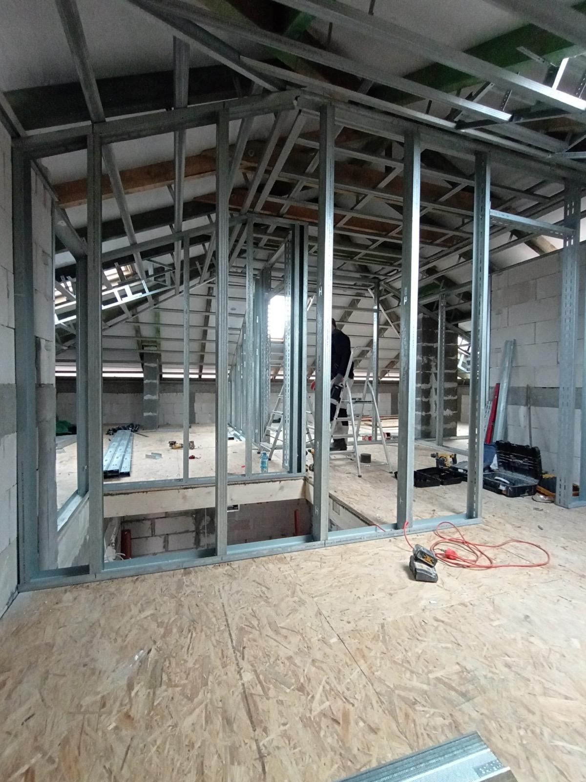 Konstrukcja ścian działowych z profili stalowych na poddaszu, widoczne narzędzia i drabina. Etap budowy z płyt karton-gips.