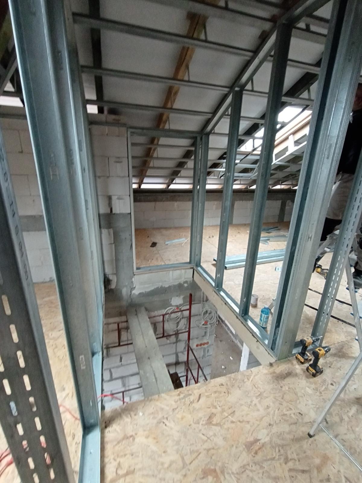 Montaż metalowej konstrukcji szkieletowej na poddaszu, widoczne profile, płyty OSB, narzędzia. Prace wykończeniowe w surowym stanie, przygotowanie do dalszych etapów.